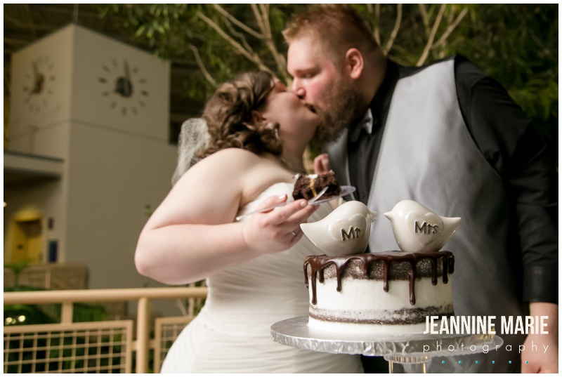 cake, bride, groom, kiss, bird cake toppers, chocolate drip cake, Woodbury Central Park, indoor wedding venue, indoor amphitheater, winter wedding, evening wedding, jewel-toned floral, Dorothy Ann Bakery, Green Mill Catering, Wedding Connection, Black Suit, Steve Madden, intimate wedding, Jeannine Marie Photography, Saint Paul wedding photographer, Minnesota wedding photographer