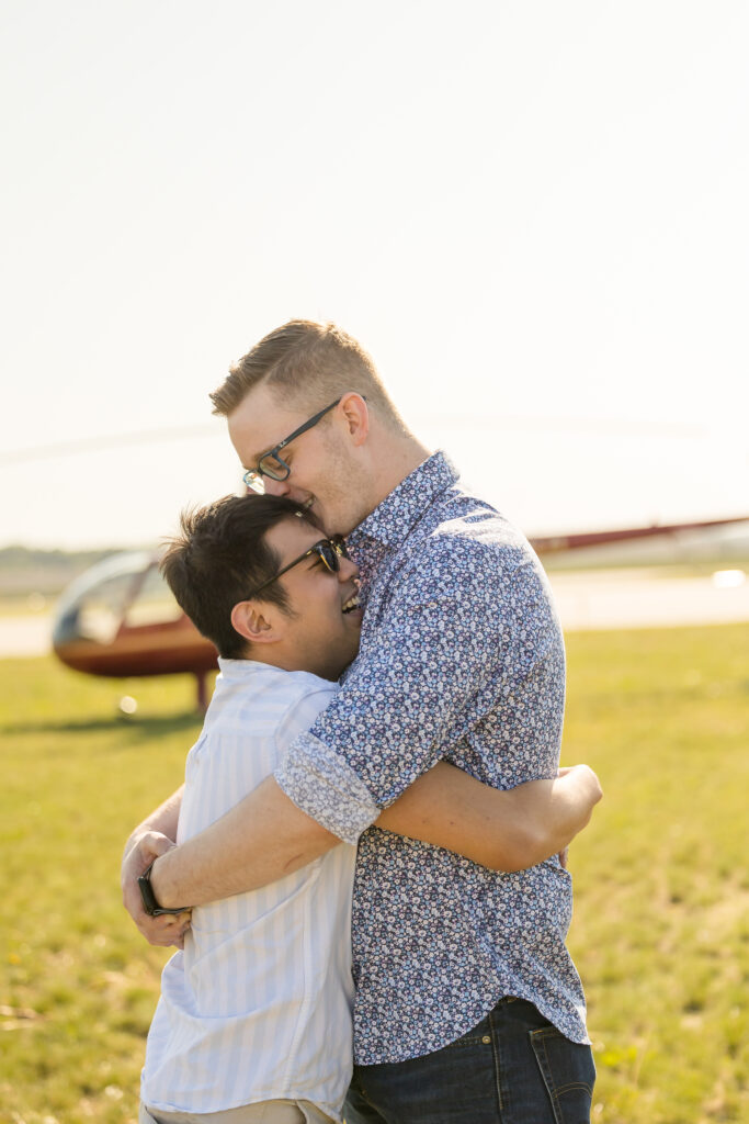 Gay couple embracing in front of a red helicopter taken by Jeannine Marie Photography.