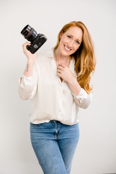 Jeannine Marie Photography posing with a camera holding her necklace